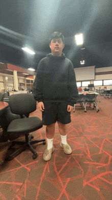 a young man wearing a black adidas hoodie and shorts stands in a room