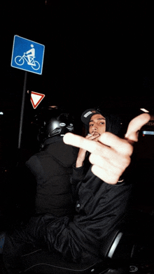 a man is giving the middle finger in front of a blue sign with a bicycle on it