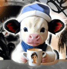 a baby cow wearing a hat and scarf is holding a cup of coffee