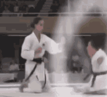 a woman in a white karate uniform is kneeling down next to a man in a black belt in a karate match .