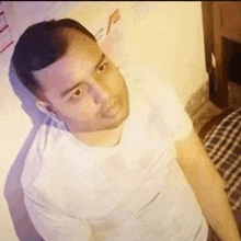 a man in a white t-shirt is standing in a room looking at the camera .