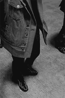 a black and white photo of a person wearing a denim jacket and black shoes with the letter s on them