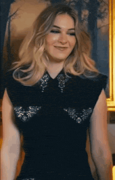 a woman in a black dress is standing in front of a painting and smiling .