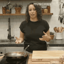 a woman in a black shirt is standing in front of a stove and a cutting board that says " munchies " on it