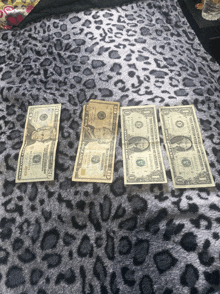 four dollar bills on a leopard print surface