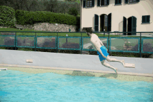 a man in blue shorts jumps into a pool