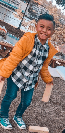 a young boy wearing a plaid shirt and a yellow jacket is holding a wooden block