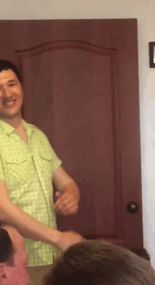 a man in a green shirt stands in front of a brown door