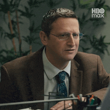a man in a suit and tie is sitting at a desk with a hbo max logo in the background