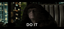 a man in a hooded robe is sitting in a chair with the words `` do it '' written on the screen .