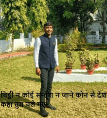 a man in a blue vest is standing in the grass in a garden .