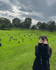 a woman covering her face with her hands in front of a cemetery full of graves