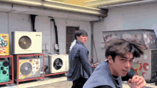 two young men are standing in front of a stack of air conditioners one of which says ' gmc ' on it