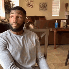 a man in a grey shirt sits in a chair in front of a table with a hand sanitizer on it