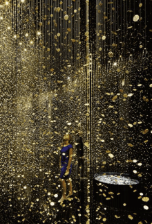 a woman in a blue dress is standing in a room filled with gold coins