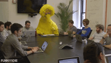a group of people are sitting around a table with a yellow sesame street character in the background