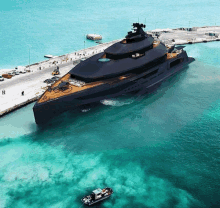 an aerial view of a large black yacht in the ocean next to a small boat .