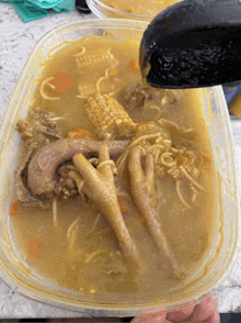 a container of soup with chicken feet corn and noodles