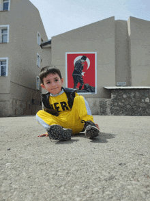 a young boy wearing a yellow shirt that says her is sitting on the ground