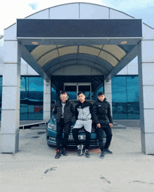 three boys pose in front of a blue car with license plate number a 08