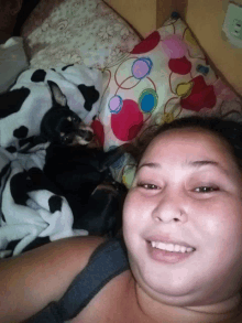 a woman laying on a bed with a small dog on her chest