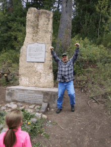 a man in a plaid shirt stands in front of a large stone with a plaque on it that says " a legend "