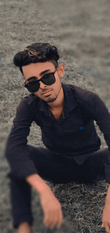 a young man wearing sunglasses and a black shirt is kneeling on the ground