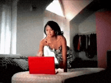 a woman is sitting on a bed using a red laptop .