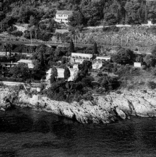 a black and white photo of a house on a cliff overlooking a body of water