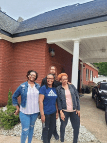 three women are posing for a picture in front of a red brick building one of them is wearing an adidas shirt