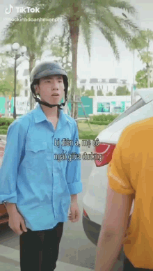 a man wearing a helmet and a blue shirt is standing in front of a car and talking to another man