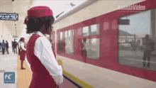 a woman in a red and white uniform is standing next to a red train with a sign in the background that says xinhuavideo