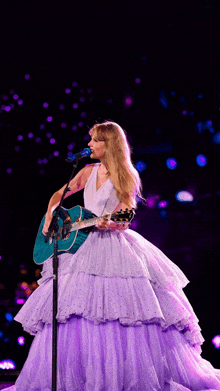 a woman in a purple dress is singing into a microphone while holding a guitar on stage .