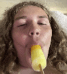 a close up of a person eating a yellow popsicle with their eyes closed