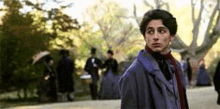 a young man in a suit and scarf is standing in a park .