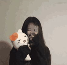 a woman is taking a selfie with her phone while holding a stuffed cat .