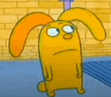 a yellow cartoon character with orange ears is standing in front of a yellow brick wall .