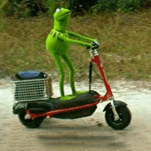 a kermit the frog is riding a scooter on a dirt road .