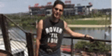 a man in a black tank top is standing on a railing overlooking a river .