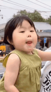 a little girl in a green dress is making a funny face and sticking her tongue out .
