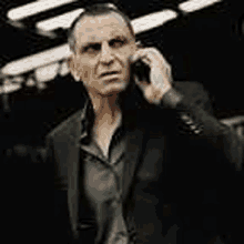 a man in a black suit is talking on a cell phone .