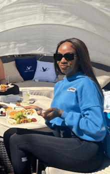 a woman in a blue sweatshirt is sitting at a table with a plate of food