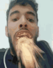 a man with a beard is eating a piece of food with his mouth wide open .