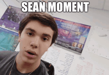 a young man taking a selfie in front of a poster that says " sean moment "