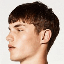 a close up of a young man 's face with a short hairstyle .