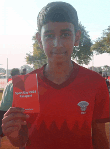 a young boy in a red shirt is holding a sport day passport