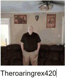 a man in a black shirt is standing in front of a couch with his hands in his pockets under a ceiling fan