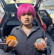 a man with pink hair and horns is holding an orange and a cantaloupe .