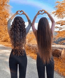 two women are standing next to each other making a heart shape with their hands .