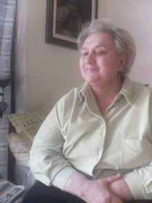 an older woman in a green shirt sits in front of a painting